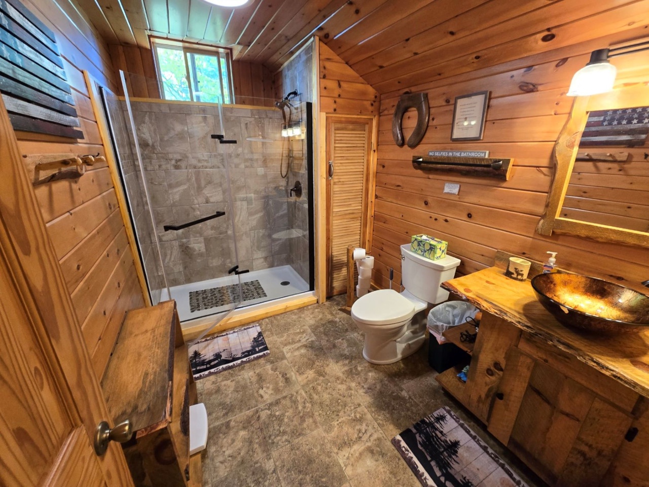 Step into your rustic bathroom retreat where warm wood meets modern amenities, featuring a spacious stone shower and stunning copper vessel sink.