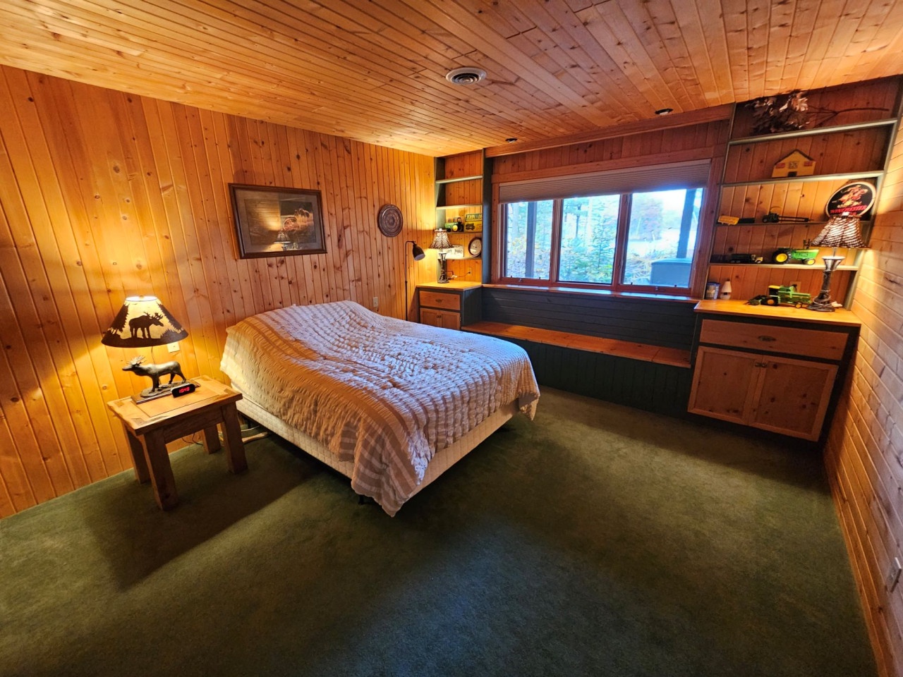 Unwind in your cozy cabin bedroom surrounded by warm wood paneling, featuring built-in storage and peaceful forest views through the window.