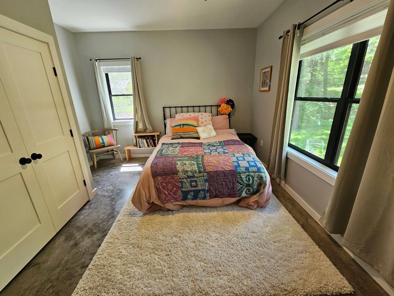 Your cozy bedroom features a comfortable bed with colorful quilted bedding and peaceful garden views through bright windows.