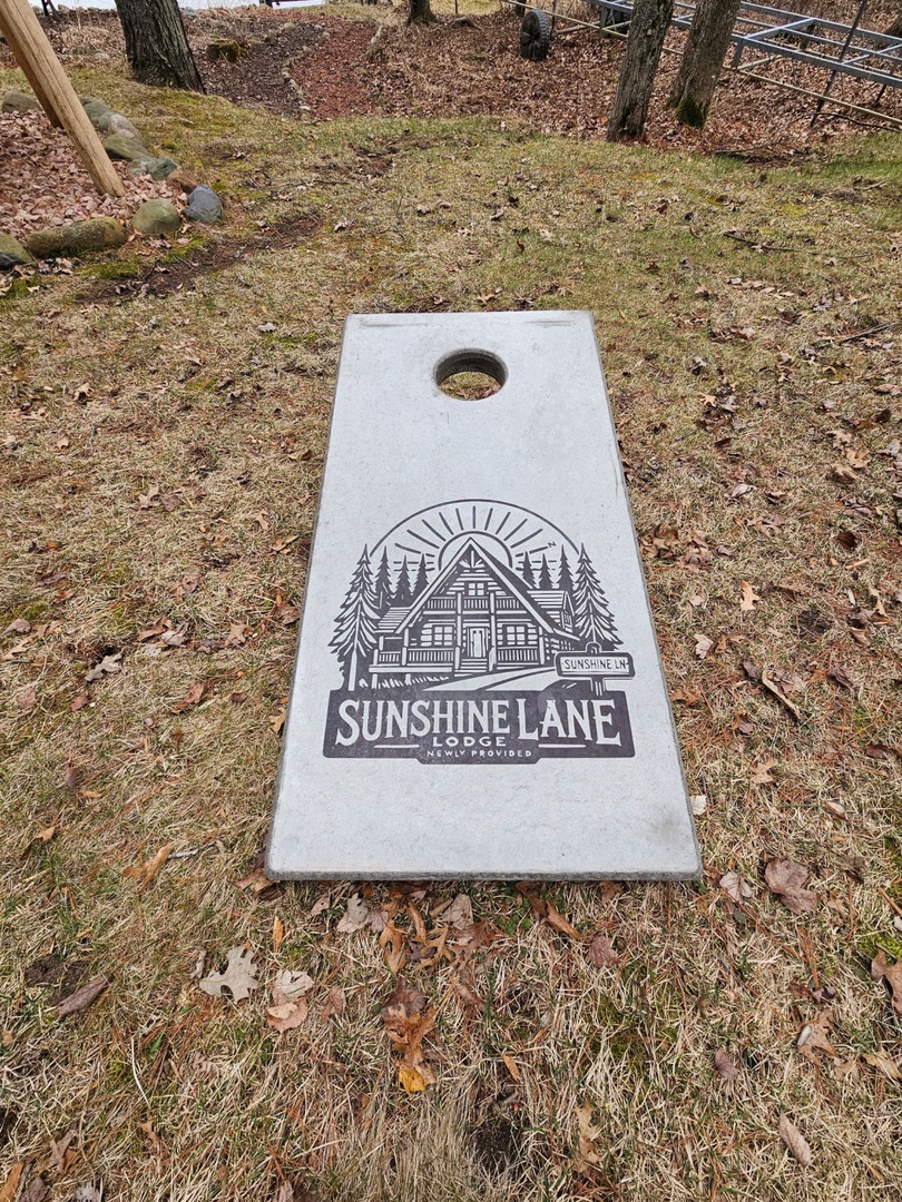 Custom cornhole board with Sunshine Lane Lodge branding sits ready for outdoor games in the property's yard.