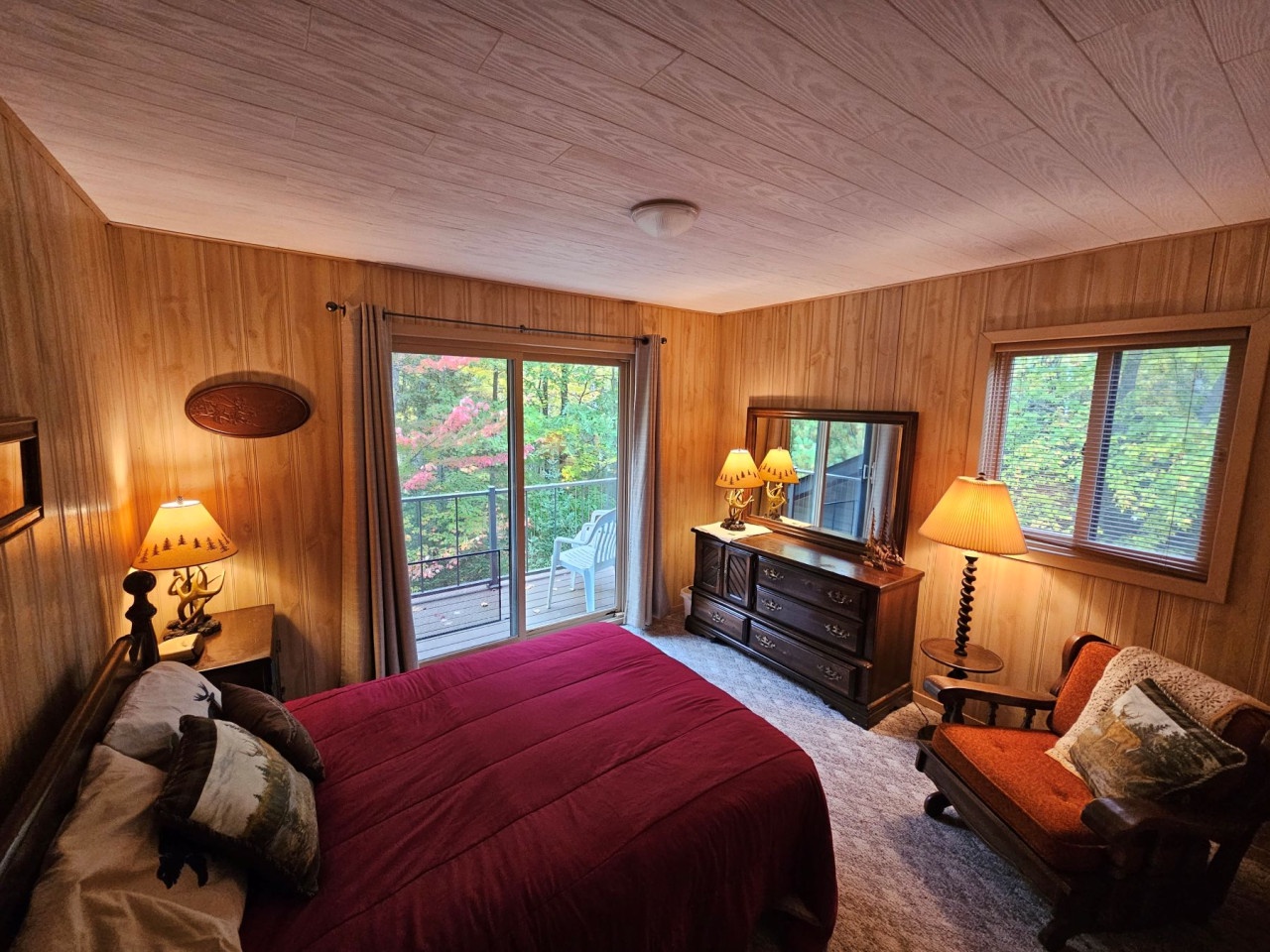 Relax in your cozy wood-paneled bedroom with warm lighting, comfy seating, and direct access to your private balcony overlooking the trees.