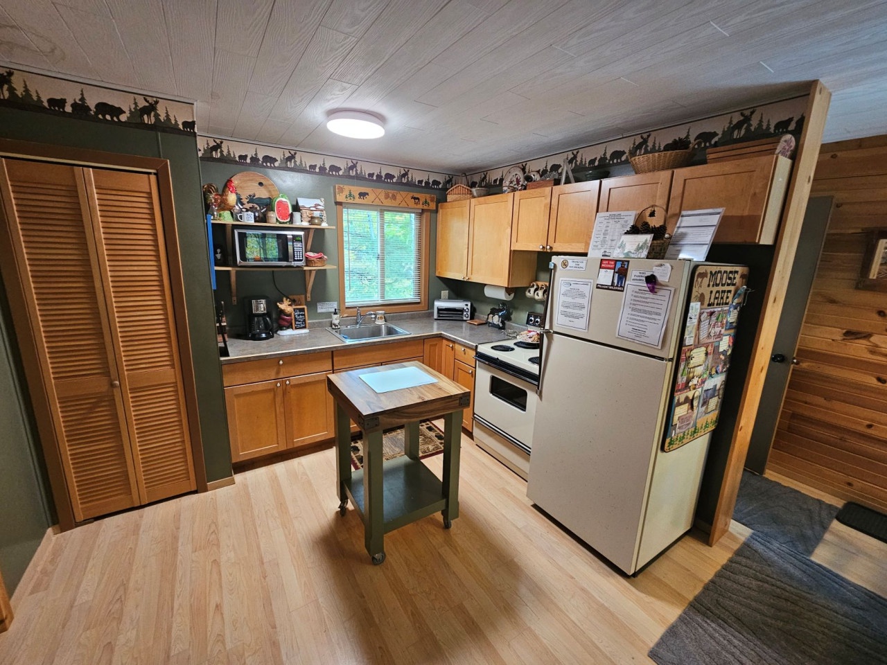 Your fully equipped kitchen awaits with warm wood cabinetry, full appliances, and charming wildlife-themed decor creating a cozy mountain cabin feel.