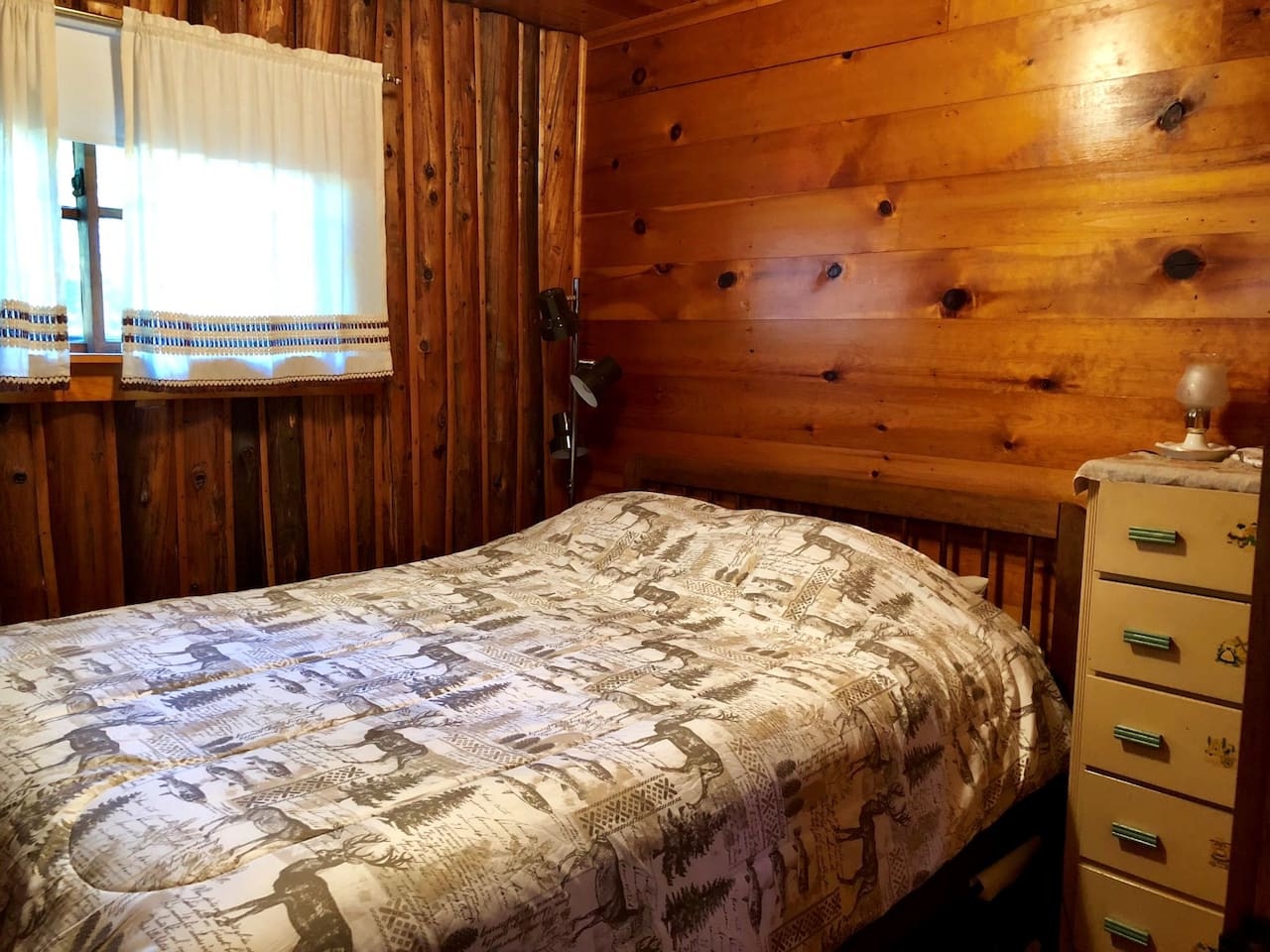 Rest peacefully in your cozy log cabin bedroom, where warm wood walls and charming vintage bedding create the perfect mountain retreat atmosphere.