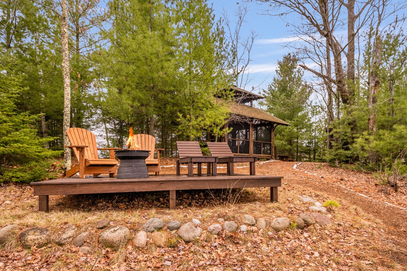 Relax on your private wooden deck with Adirondack chairs and fire pit, surrounded by towering pines and peaceful forest views.