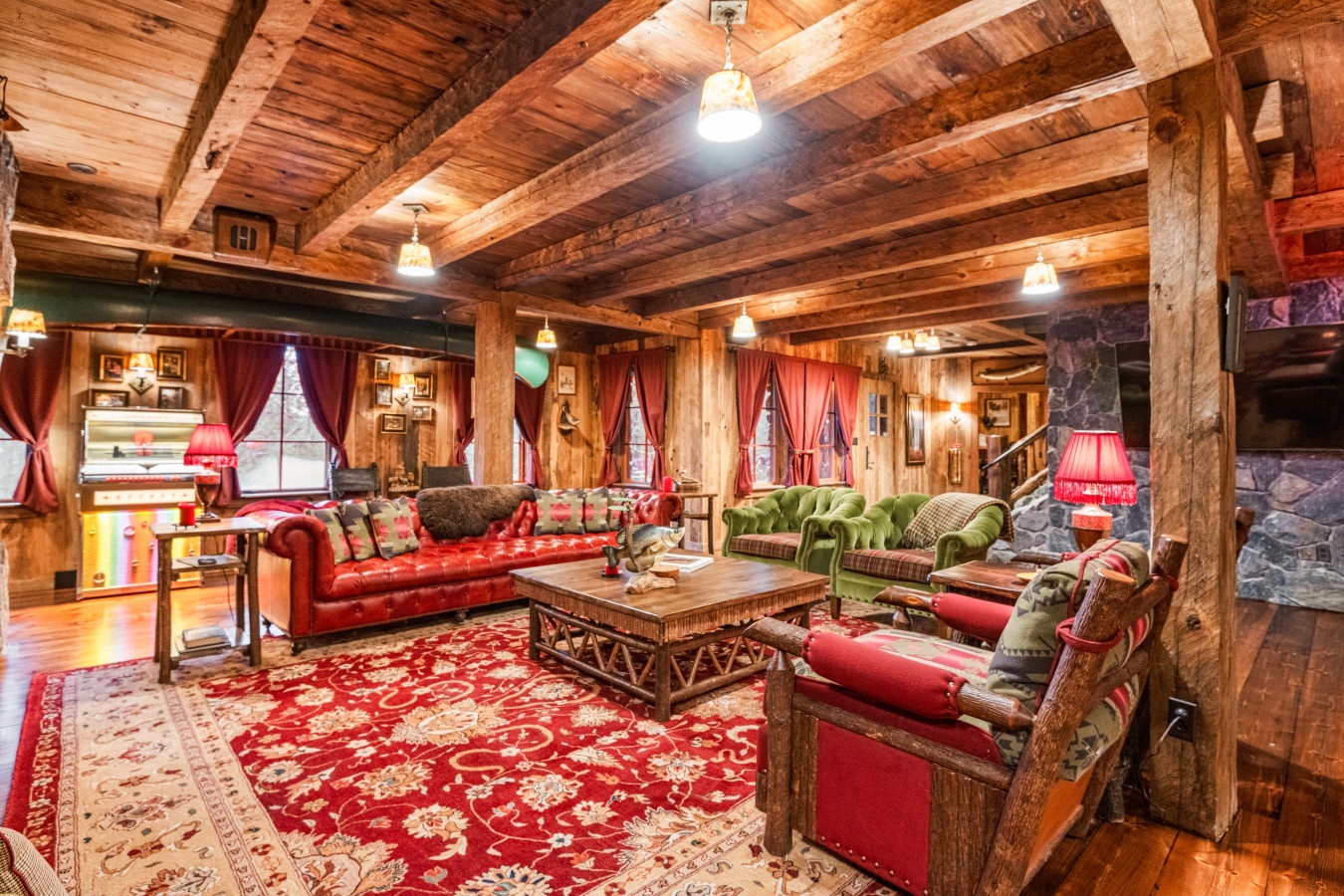Sink into this majestic lodge living room where rustic timber beams frame plush leather seating and a grand stone fireplace creates your perfect mountain retreat.