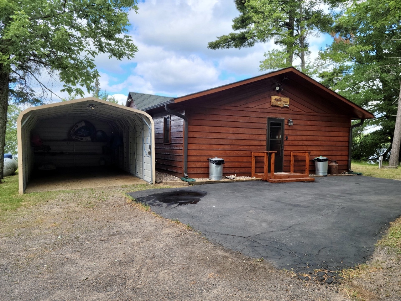 Rustic lakefront cabin with covered parking and welcoming front entrance surrounded by mature trees and peaceful natural setting.