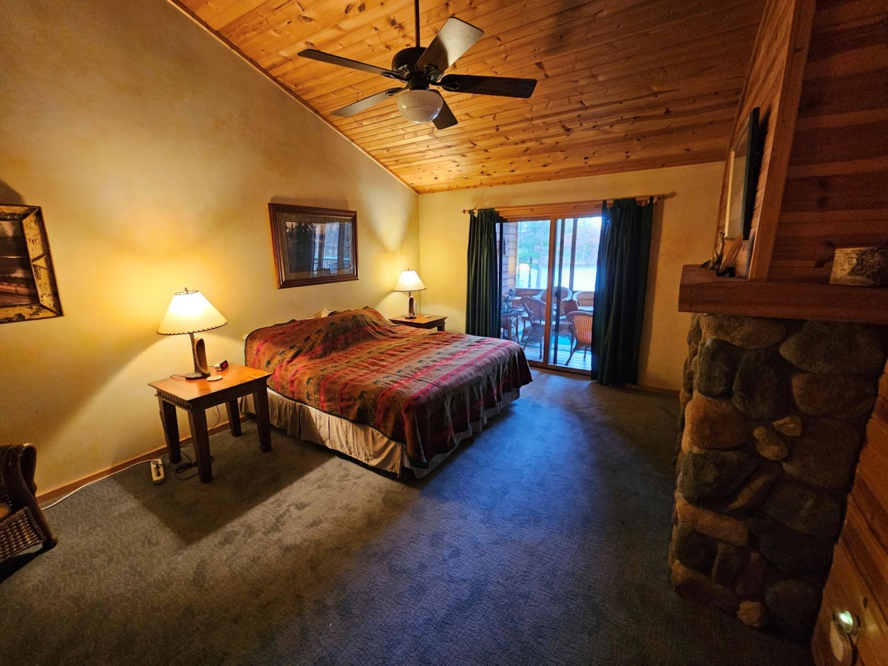 Cozy up in your rustic bedroom featuring warm wood ceilings, a stone fireplace, and private balcony access for peaceful mountain mornings.