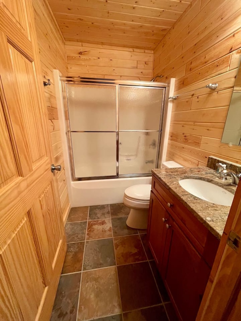 Unwind in this rustic bathroom with rich wood walls and modern granite countertops offering the perfect blend of cabin charm.