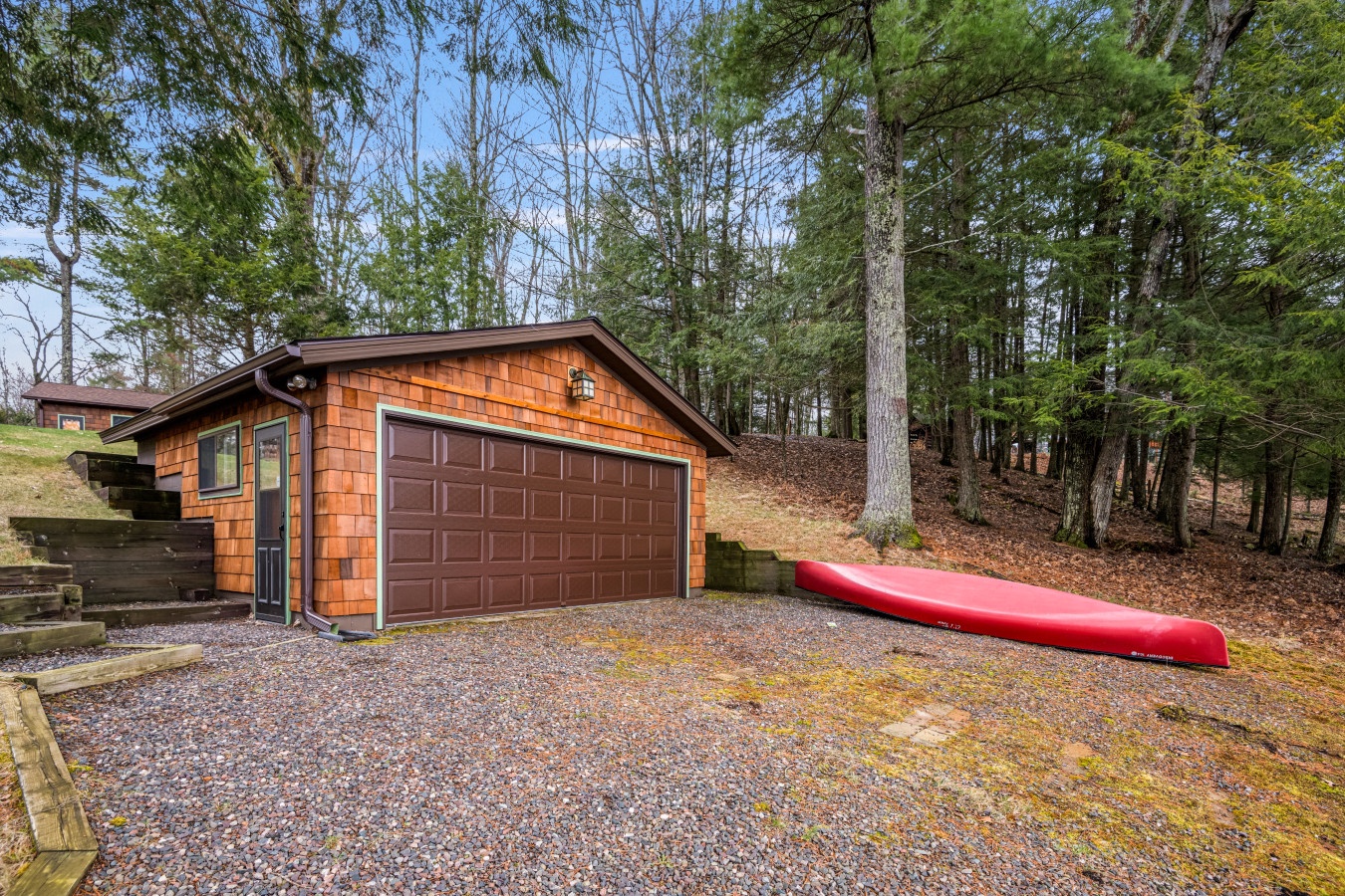 Nestled in the woods, this charming cedar-sided garage offers secure parking with red kayaks ready for your next adventure.