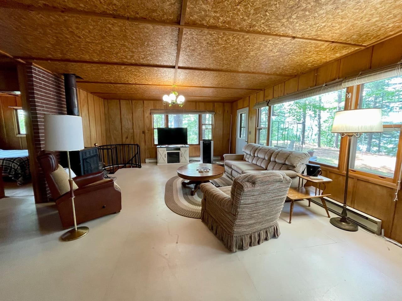 Unwind in your cozy wood-paneled retreat with comfortable seating, warm fireplace, and peaceful forest views through panoramic windows.