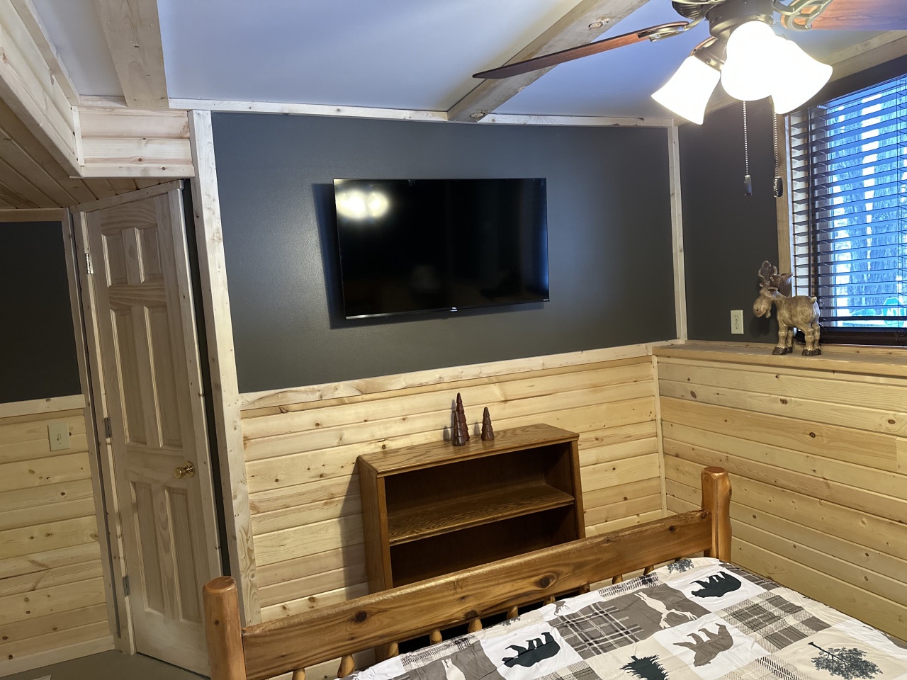 Cozy up in your rustic cabin bedroom with natural wood walls and mounted TV for relaxing evenings after mountain adventures.