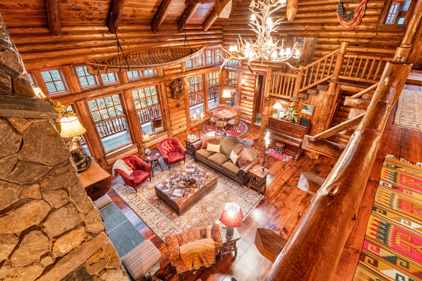 Cozy up in this stunning log cabin living room with soaring ceilings, antler chandelier, stone fireplace, and plush seating perfect for mountain evenings.