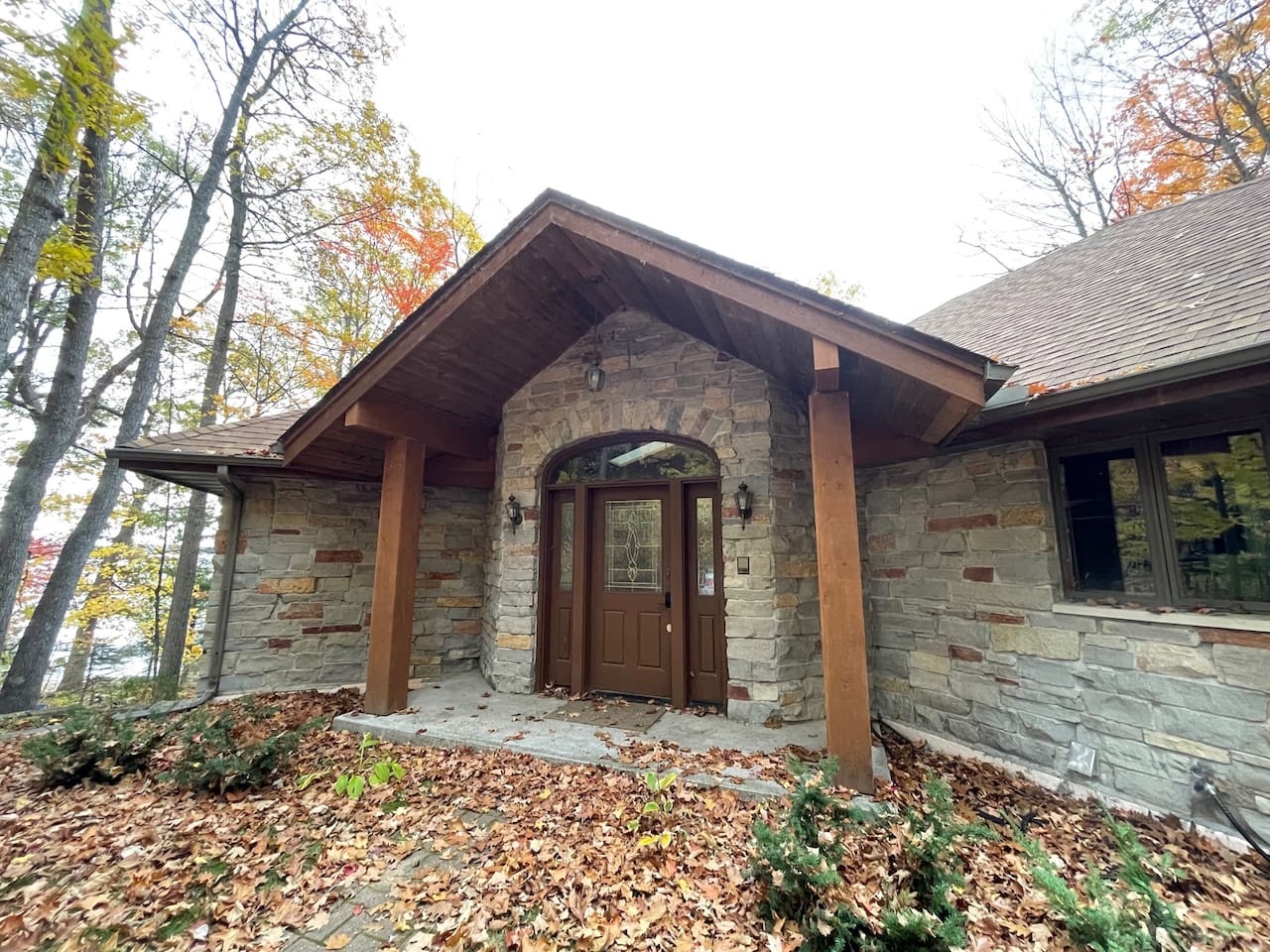Natural stone facade with timber accents creates an inviting entrance nestled among autumn trees.
