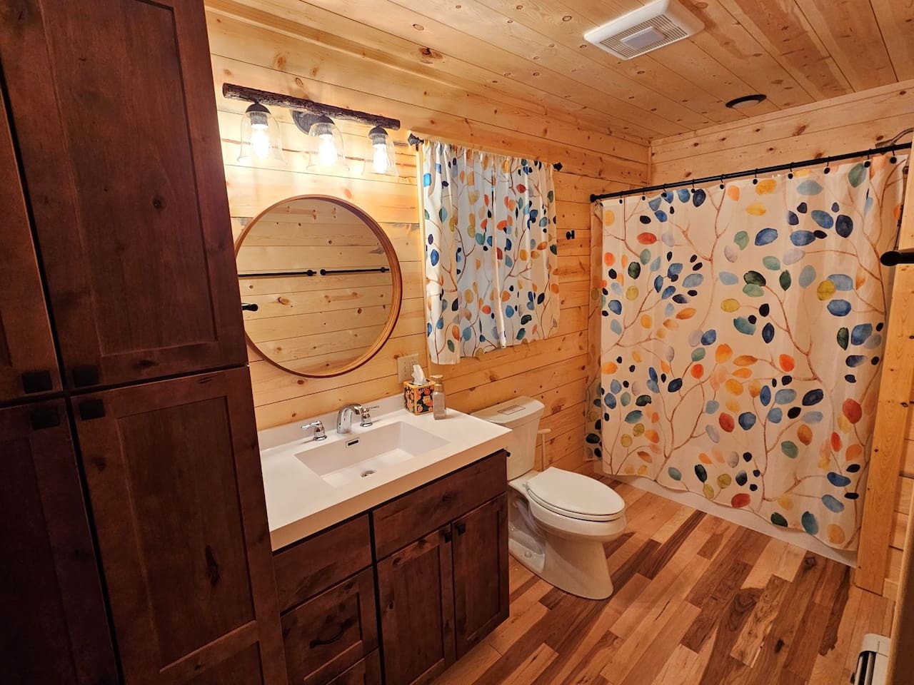 Refresh in your charming rustic bathroom with warm wood paneling, colorful artwork, and modern fixtures creating a cozy retreat.