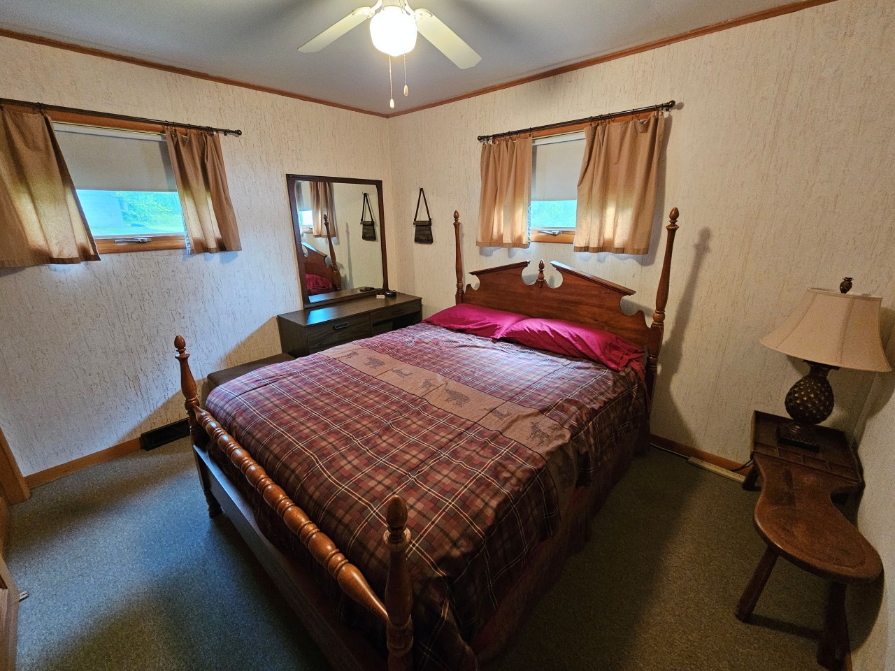 Rest peacefully in your cozy bedroom featuring a classic wooden four-poster bed, warm plaid linens, and charming antique furnishings that create a homey retreat.