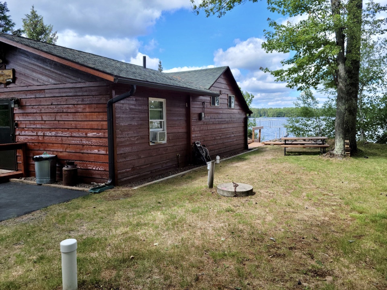 Charming lakefront cabin with rustic wooden siding nestled among tall trees, featuring outdoor seating and direct water access.