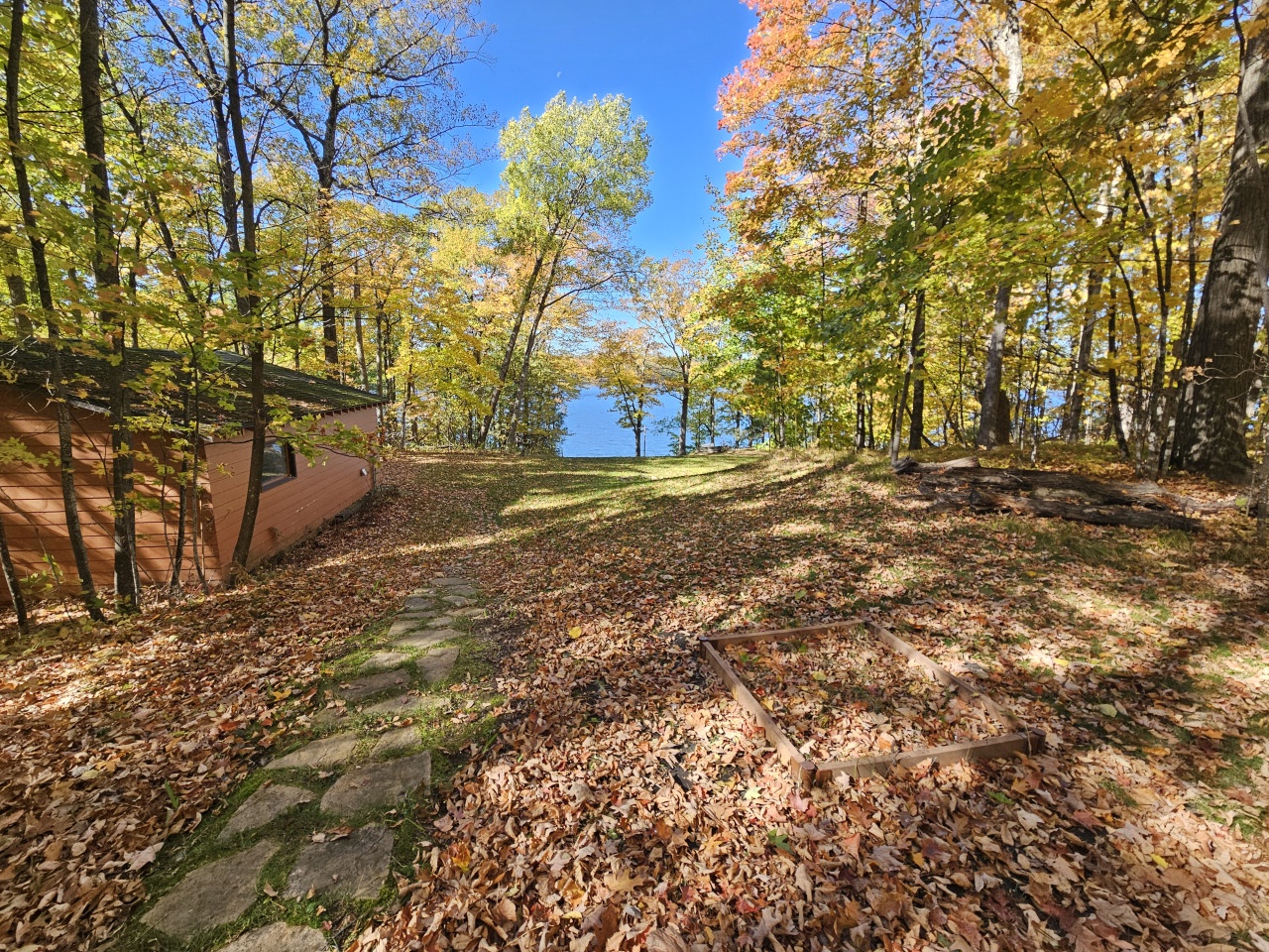 A scenic autumn trail through vibrant fall foliage leads toward peaceful lake waters, showcasing the property's natural woodland setting.