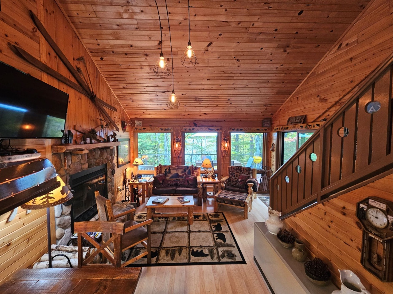 Relax in your rustic living room with stone fireplace, cozy seating, and forest views through large windows.