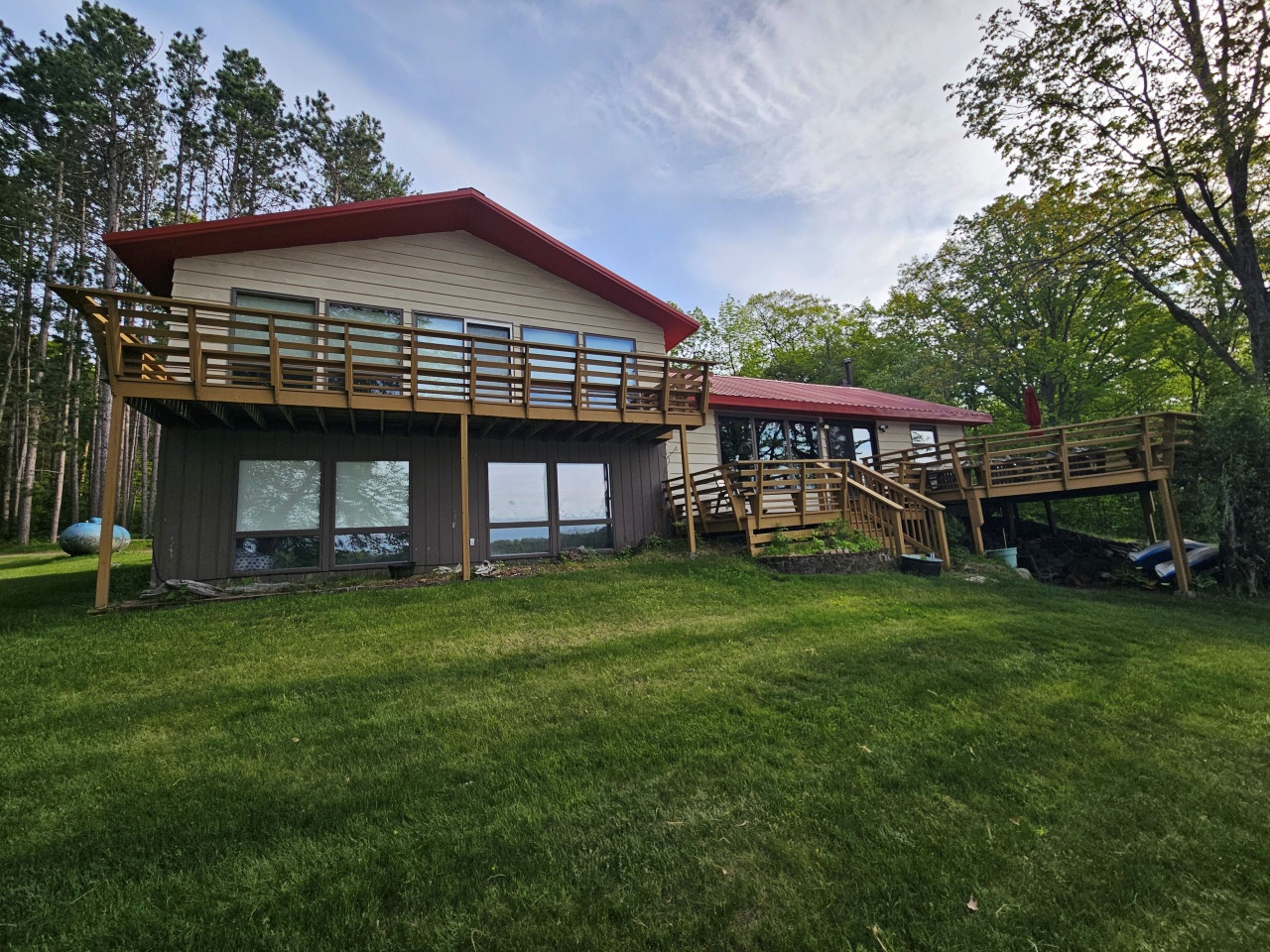 Modern lakeside retreat featuring expansive wooden decks and floor-to-ceiling windows surrounded by mature trees and manicured lawn.