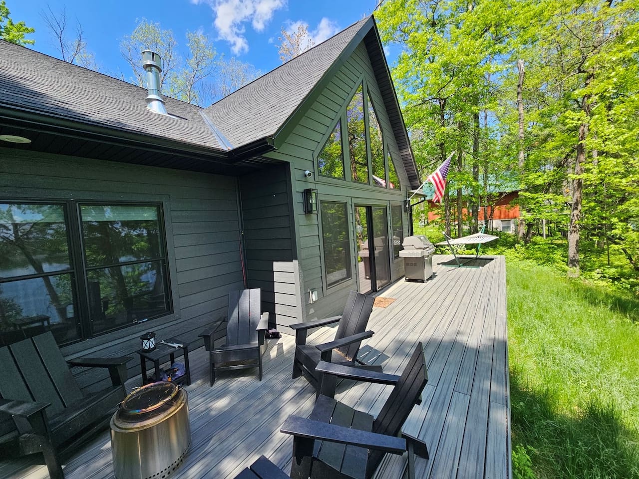 A modern cabin with striking A-frame windows and spacious deck nestled among lush spring trees, offering a perfect forest retreat.