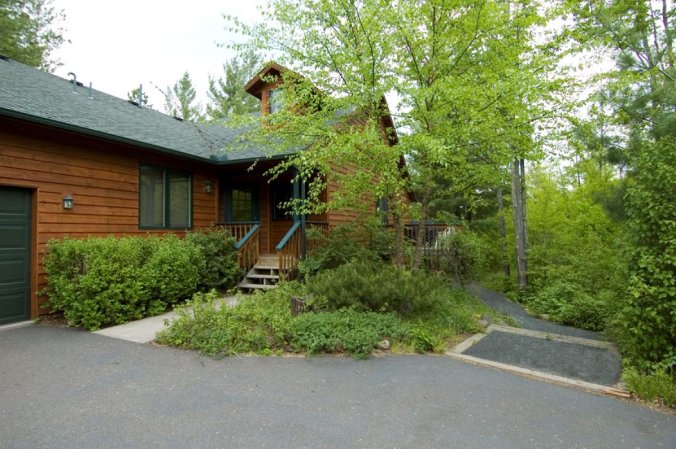 Charming log cabin nestled among mature trees with convenient paved parking and natural landscaping creating a peaceful woodland retreat setting.