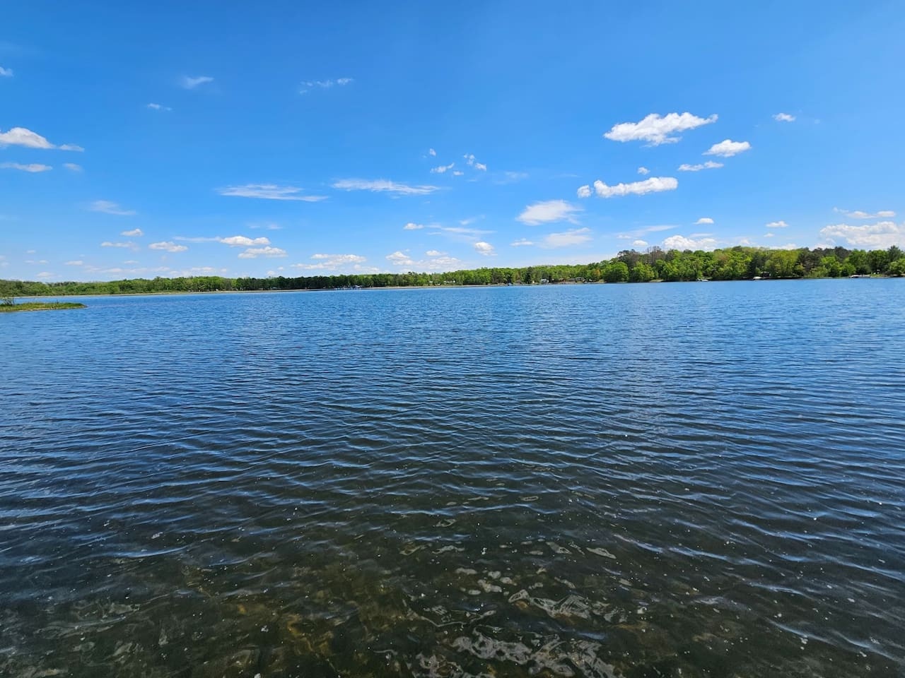 Pristine lake waters stretch toward wooded shorelines under brilliant blue skies, creating a peaceful natural setting.