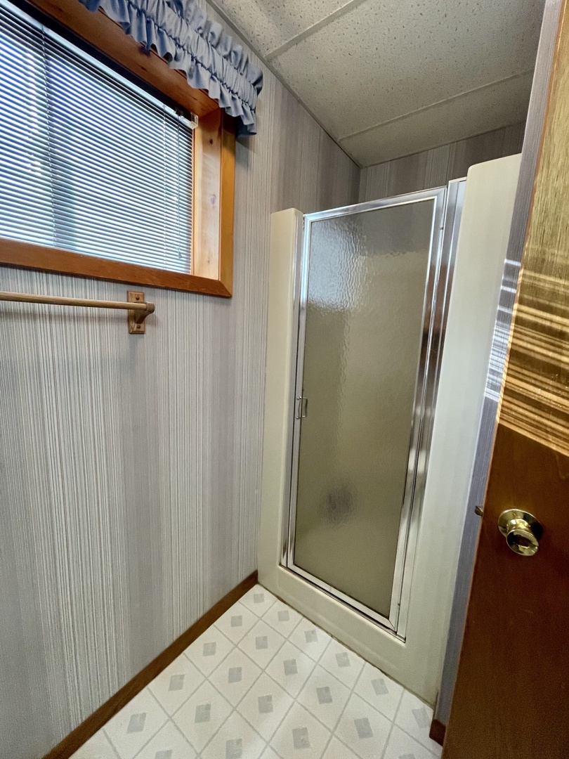 Step into your private bathroom featuring a spacious glass shower enclosure with diamond-pattern tile flooring and natural light from the window above.