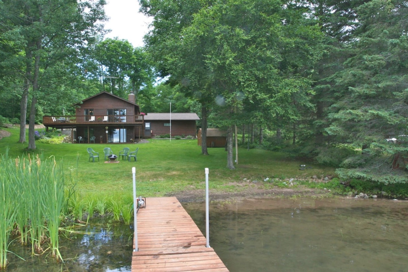 Lakefront cabin with private dock surrounded by mature trees, featuring outdoor seating and peaceful natural setting.