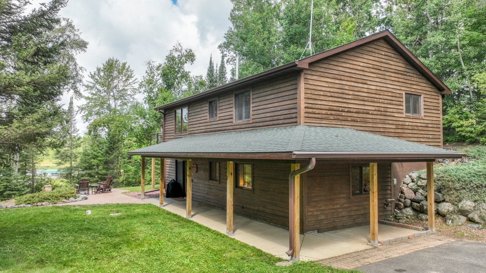 A charming two-story wooden cabin surrounded by mature trees, offering a peaceful forest retreat with covered outdoor spaces.