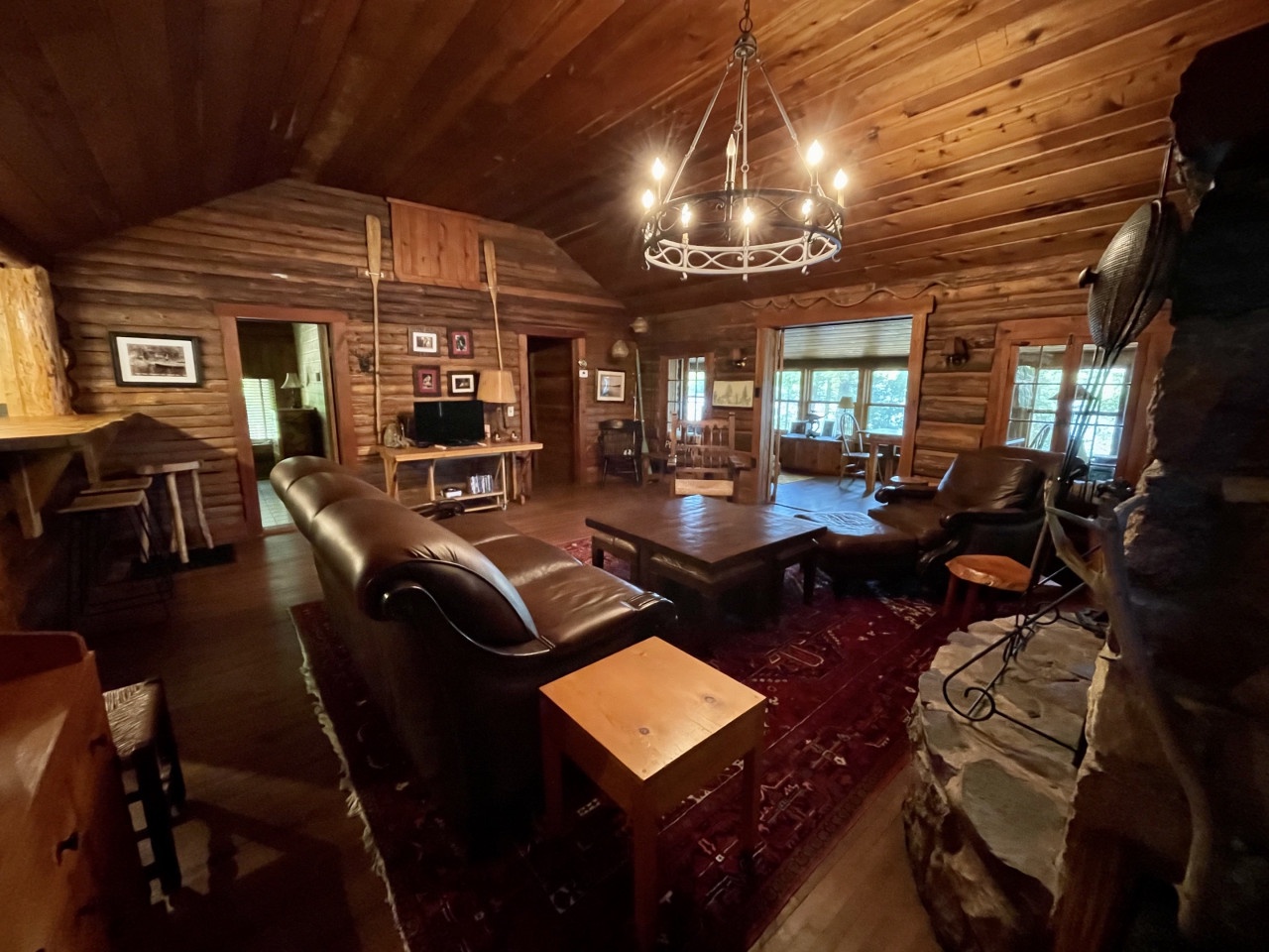 Unwind in your rustic log cabin living room, where warm wood walls, leather seating, and candlelit chandelier create the perfect mountain retreat atmosphere.