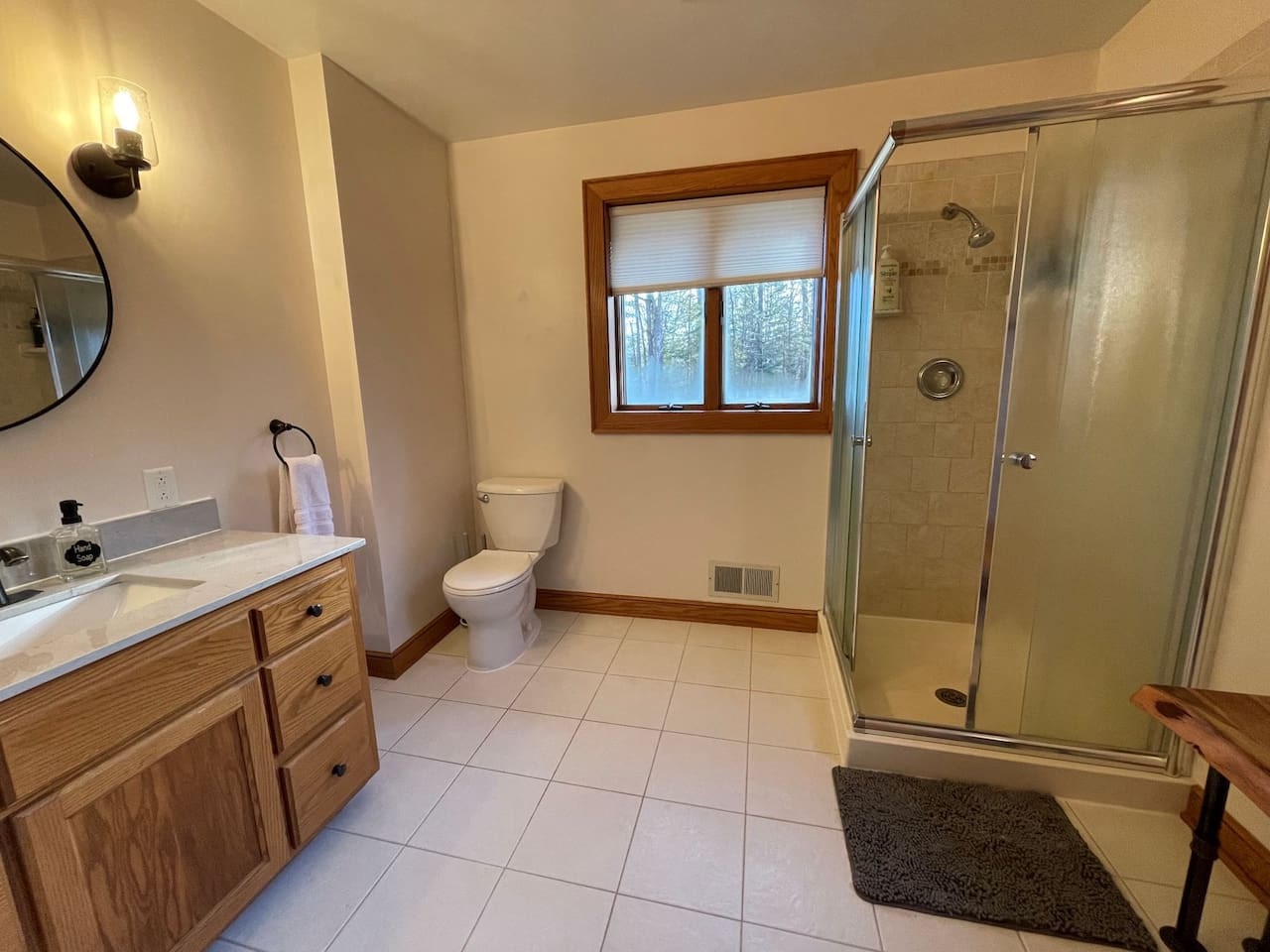 Refresh in your spacious private bathroom featuring a walk-in shower, elegant vanity, and peaceful forest views through the window.