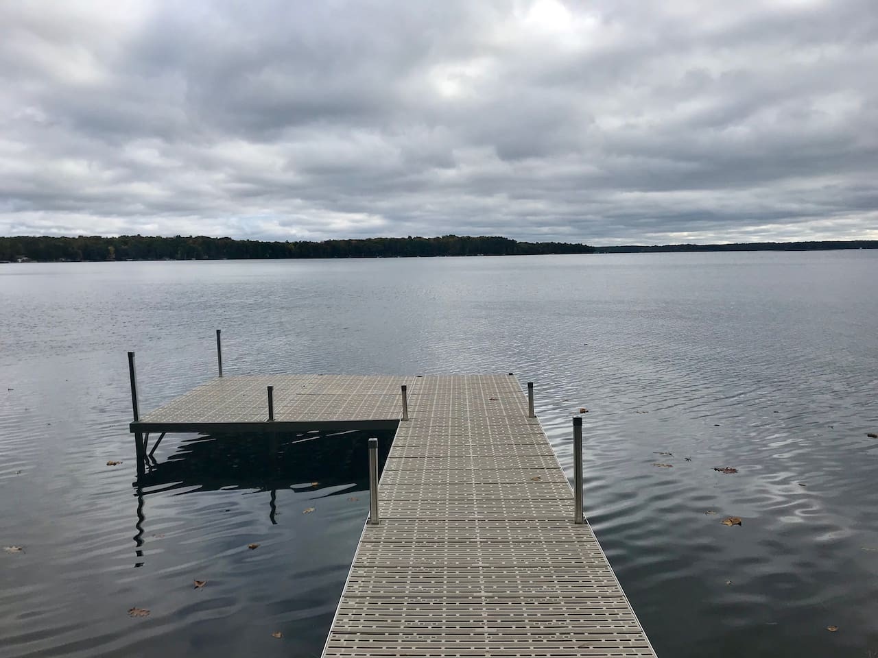 Private dock extends into the tranquil lake, surrounded by forested shores under dramatic cloudy skies.