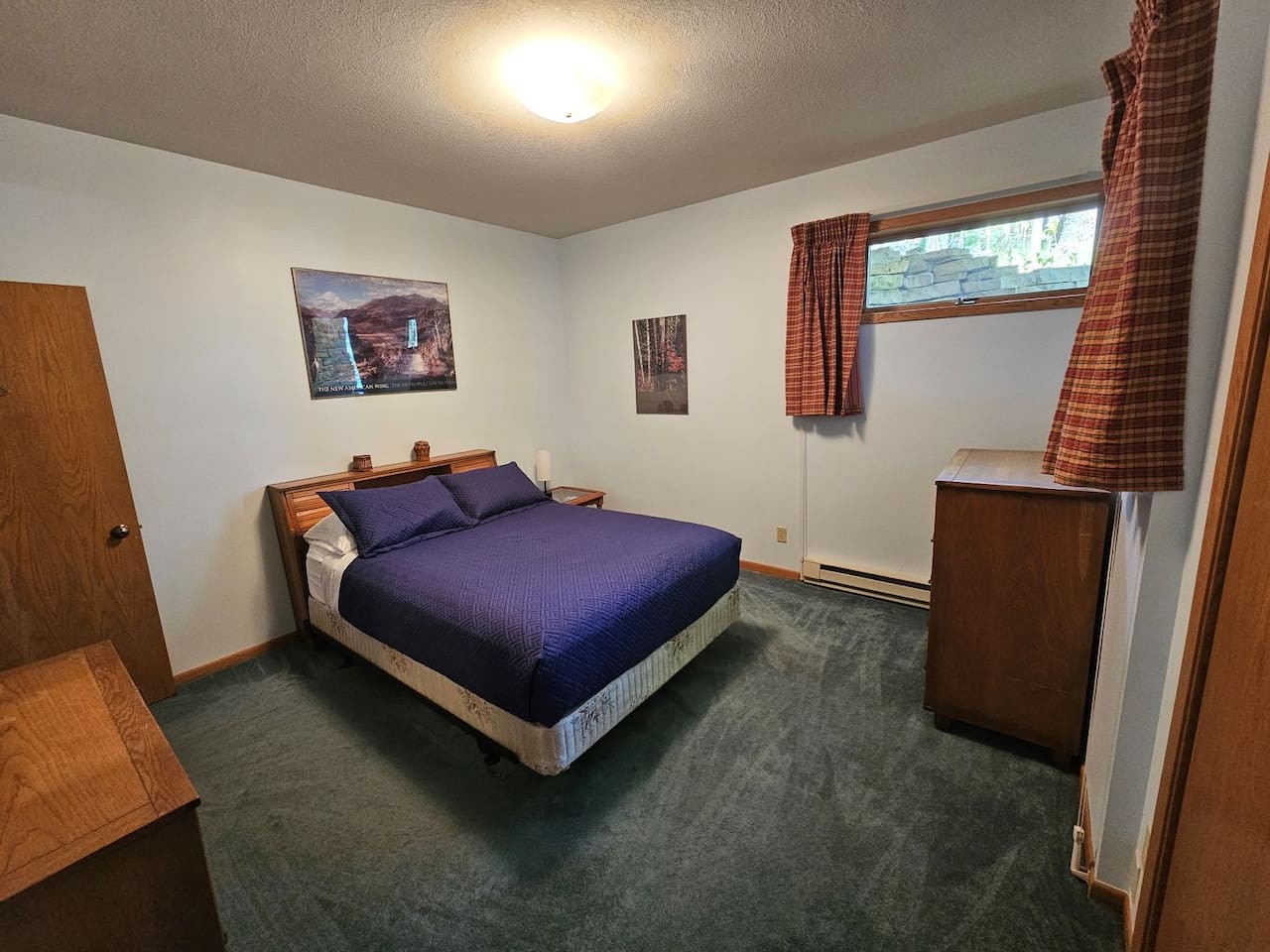 Your cozy bedroom features a comfortable queen bed with crisp linens, natural light from your window, and warm wood accents.