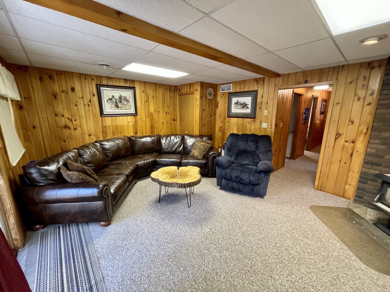 Cozy up in your private rec room featuring rustic knotty pine walls, plush leather sectional, and unique live-edge coffee table for perfect movie nights.