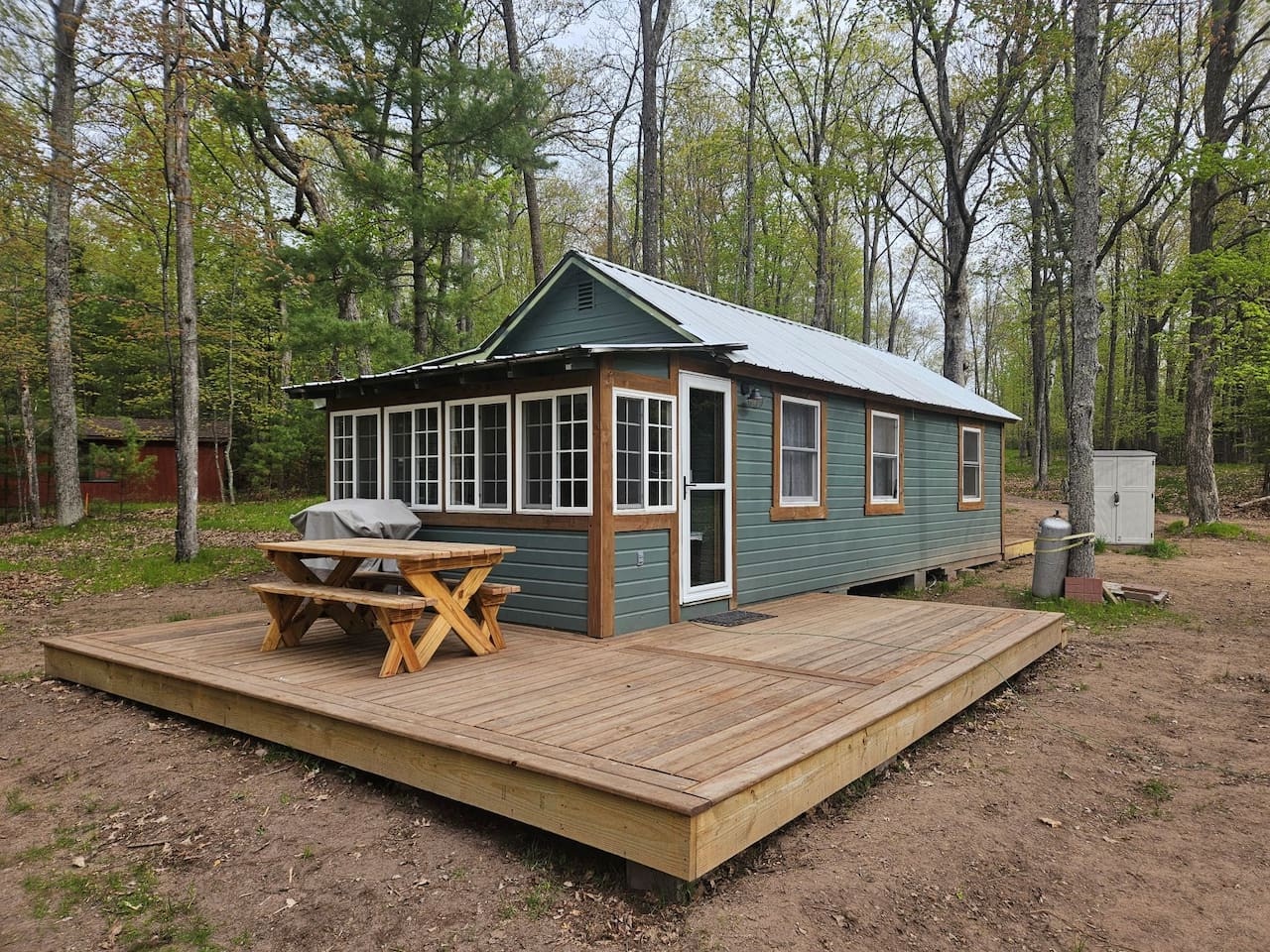 Charming lakeside cabin nestled among towering trees, featuring a spacious deck where you can dine outdoors and soak in nature's tranquility.