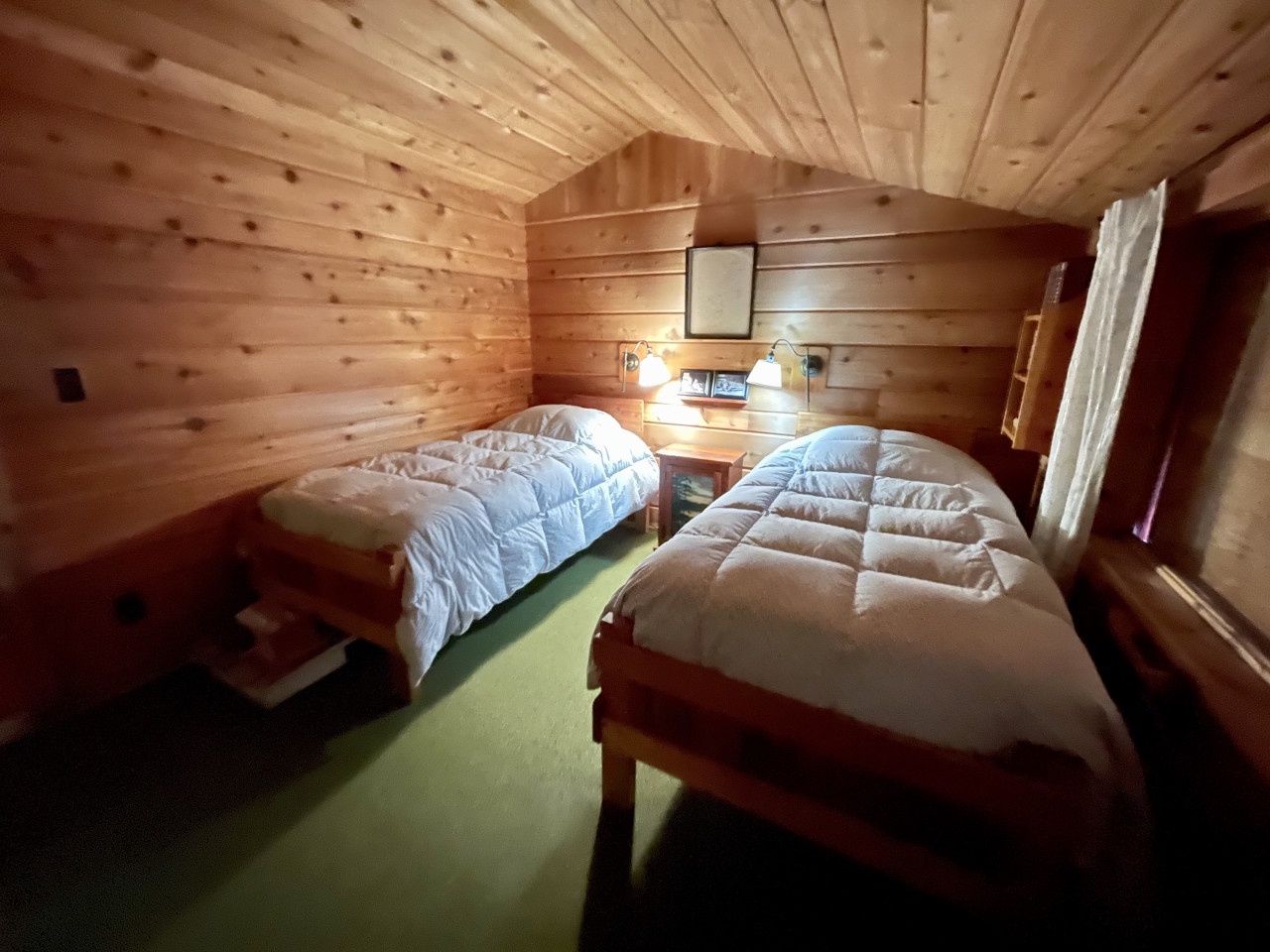 Your cozy wooden cabin bedroom features twin beds with plush comforters, perfect for restful nights surrounded by warm pine walls.