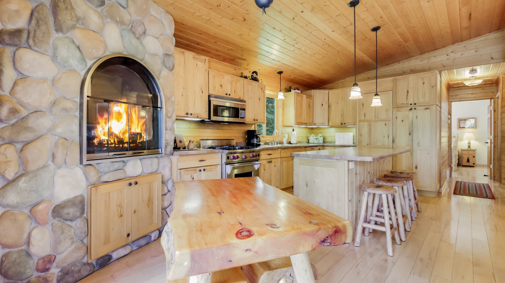 Cozy up in your rustic kitchen with a crackling stone fireplace, natural wood cabinets, and bar seating perfect for morning coffee or evening wine.