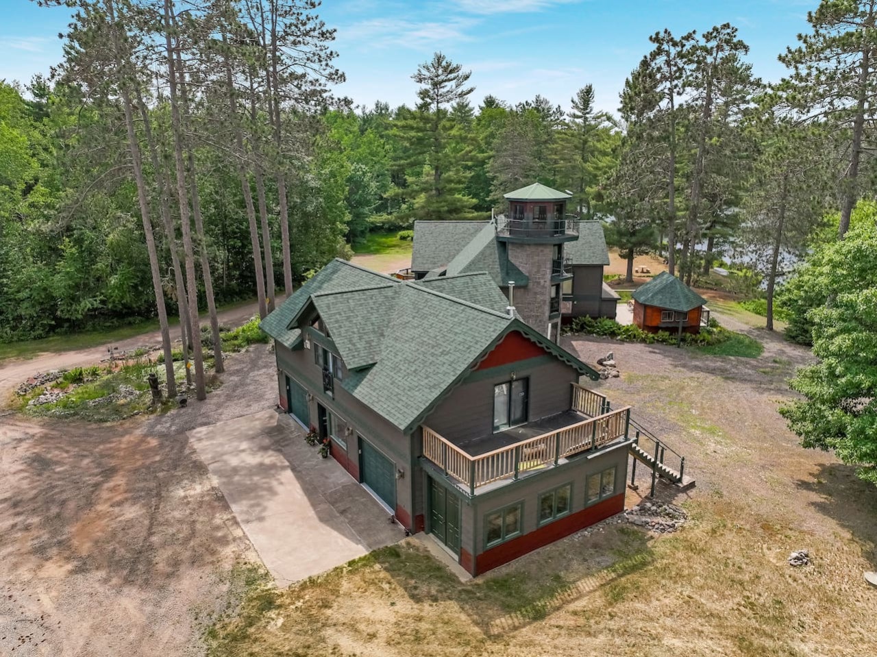 Distinctive lakefront property featuring unique architecture with tower element, surrounded by mature forest and natural landscape setting.