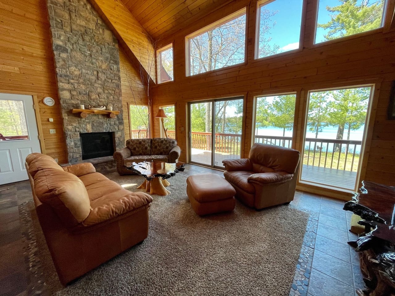 Unwind in this stunning living room with soaring ceilings, stone fireplace, and panoramic lake views through floor-to-ceiling windows.