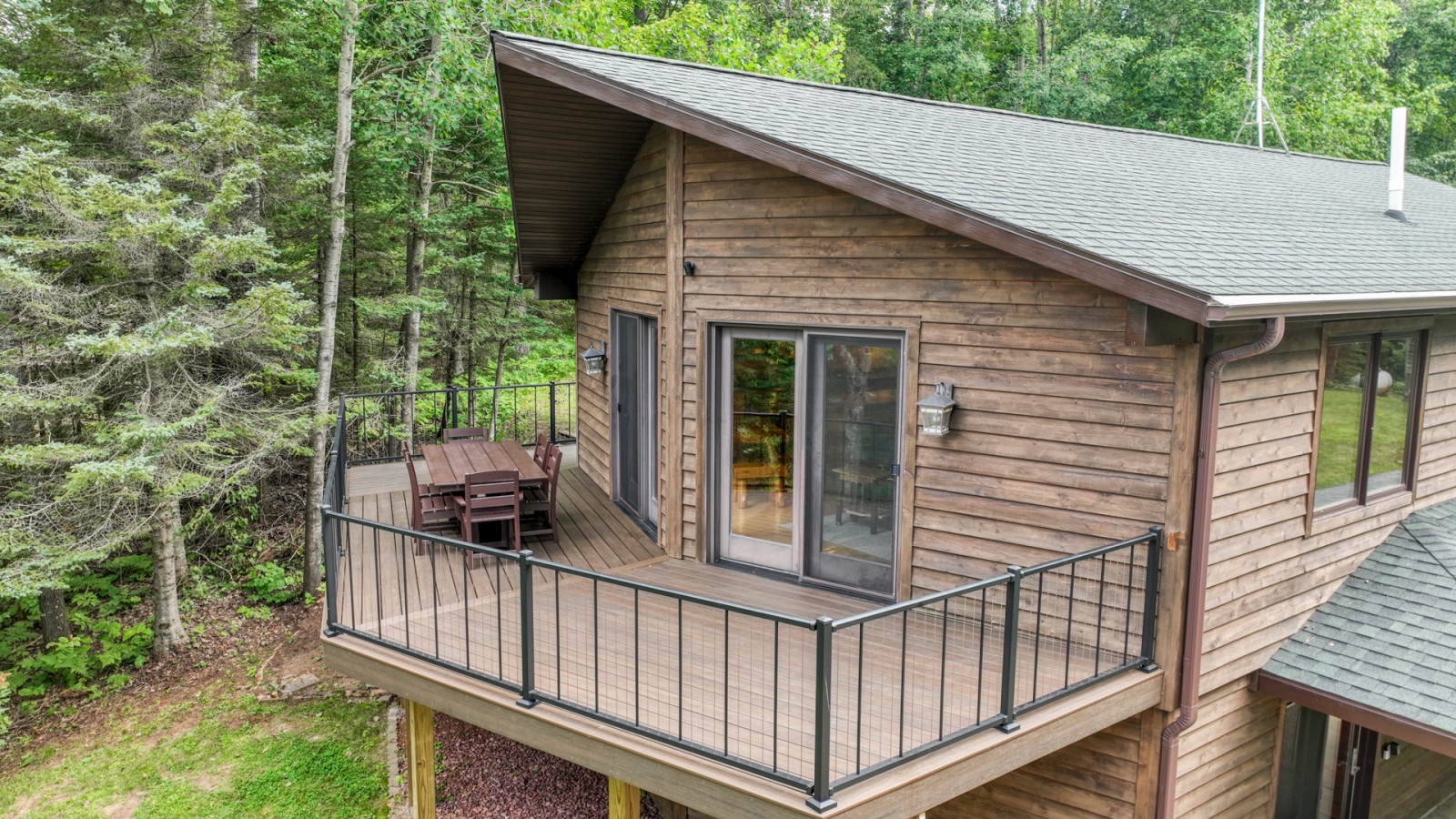 Elevated wood cabin nestled among lush forest trees, featuring a wraparound deck with outdoor seating and large windows.