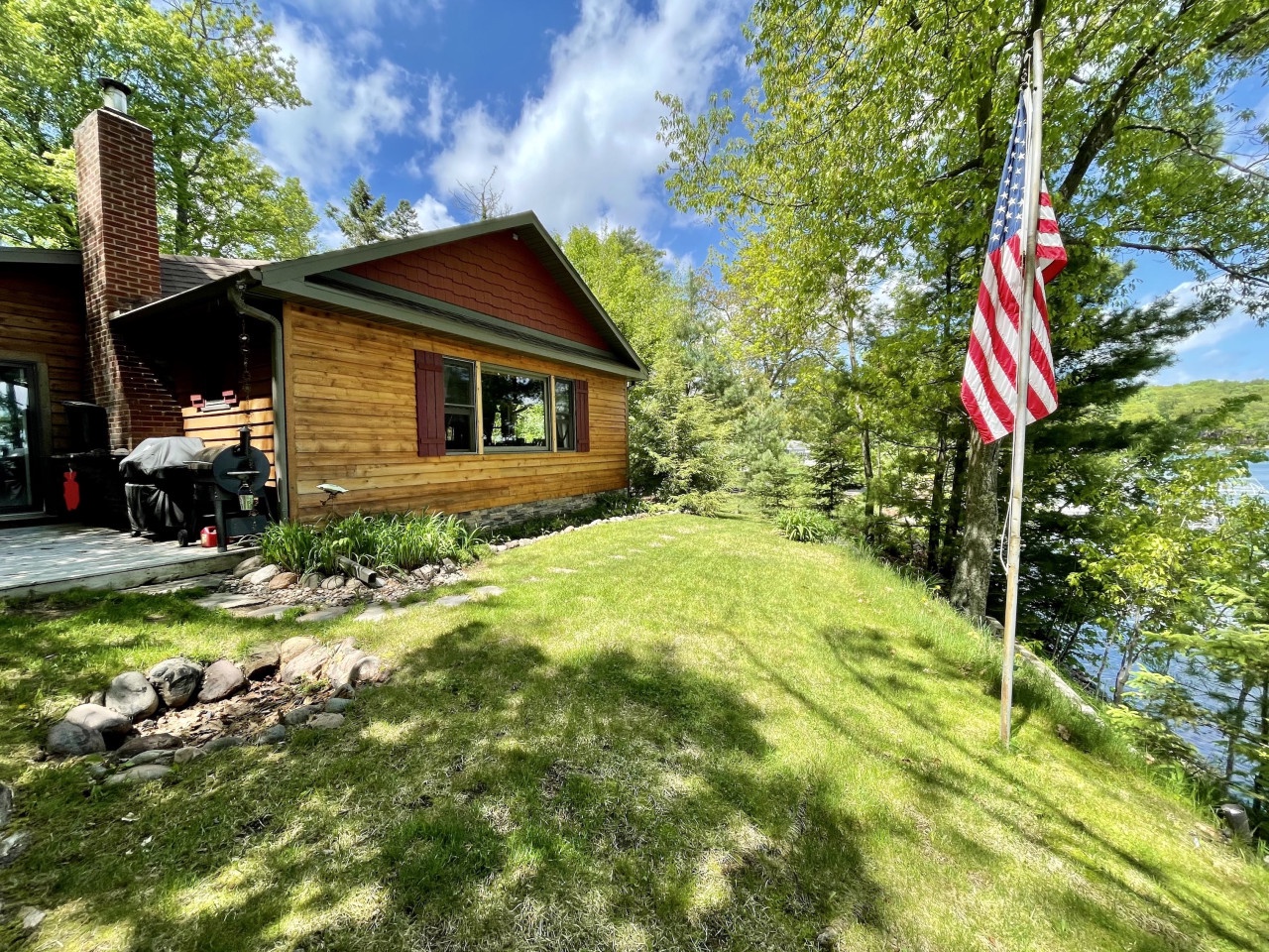 Charming lakeside cabin with American flag and pristine waterfront location surrounded by mature trees and landscaped grounds.