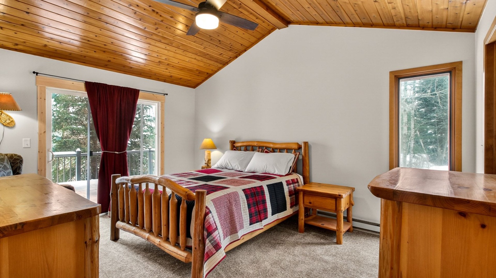 Rest in your cozy bedroom with warm wood accents, plaid bedding, and forest views through French doors leading to your private balcony.