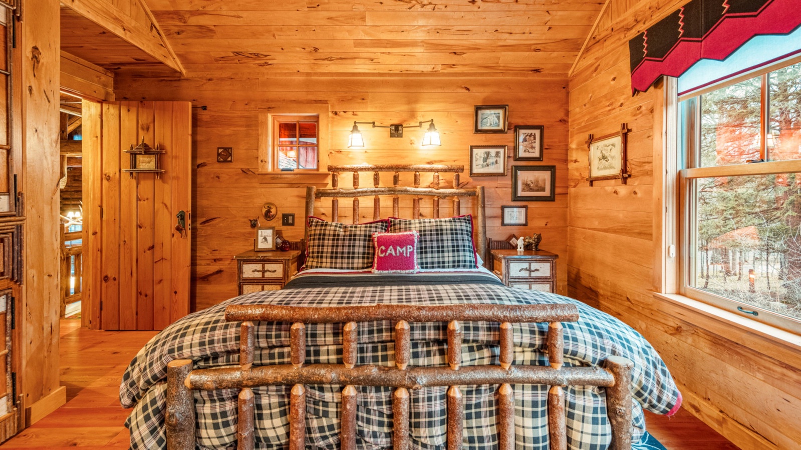 Cozy log cabin bedroom with rustic charm, plaid bedding, and forest views through large windows for your mountain retreat.