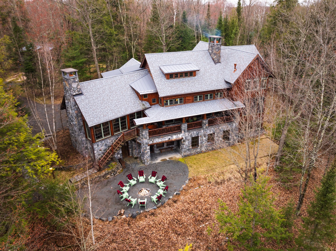 Stunning mountain lodge surrounded by forest with outdoor fire pit seating area, perfect for peaceful woodland retreat.