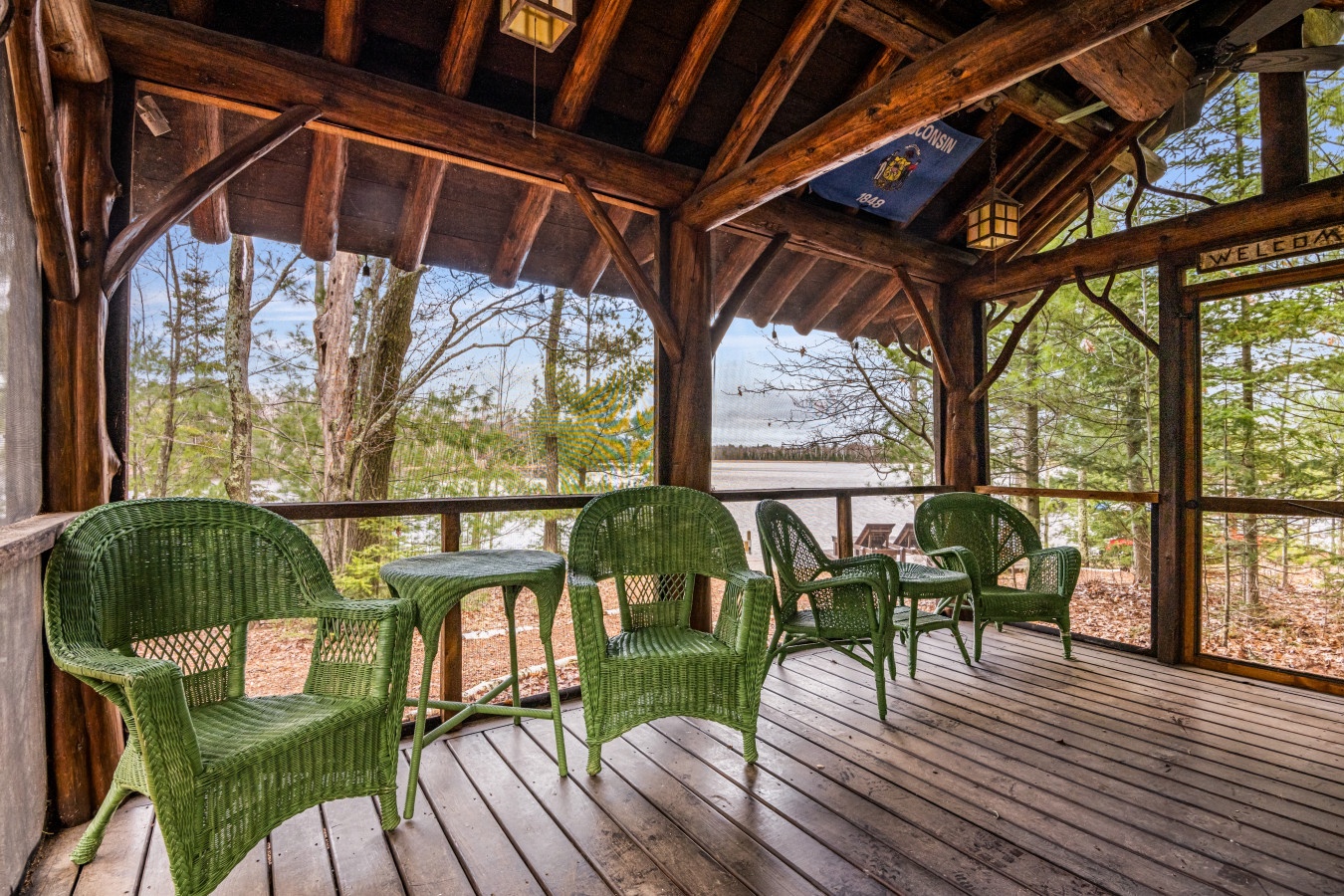 Unwind on your private screened porch where rustic charm meets comfort—green wicker seating overlooks peaceful woodland views through timber-framed openings.
