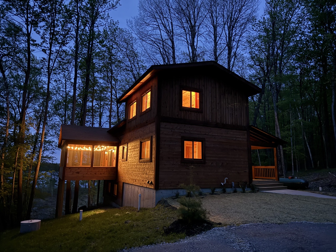 A cozy wooden cabin glows warmly at dusk, nestled among towering trees in a peaceful forest setting.