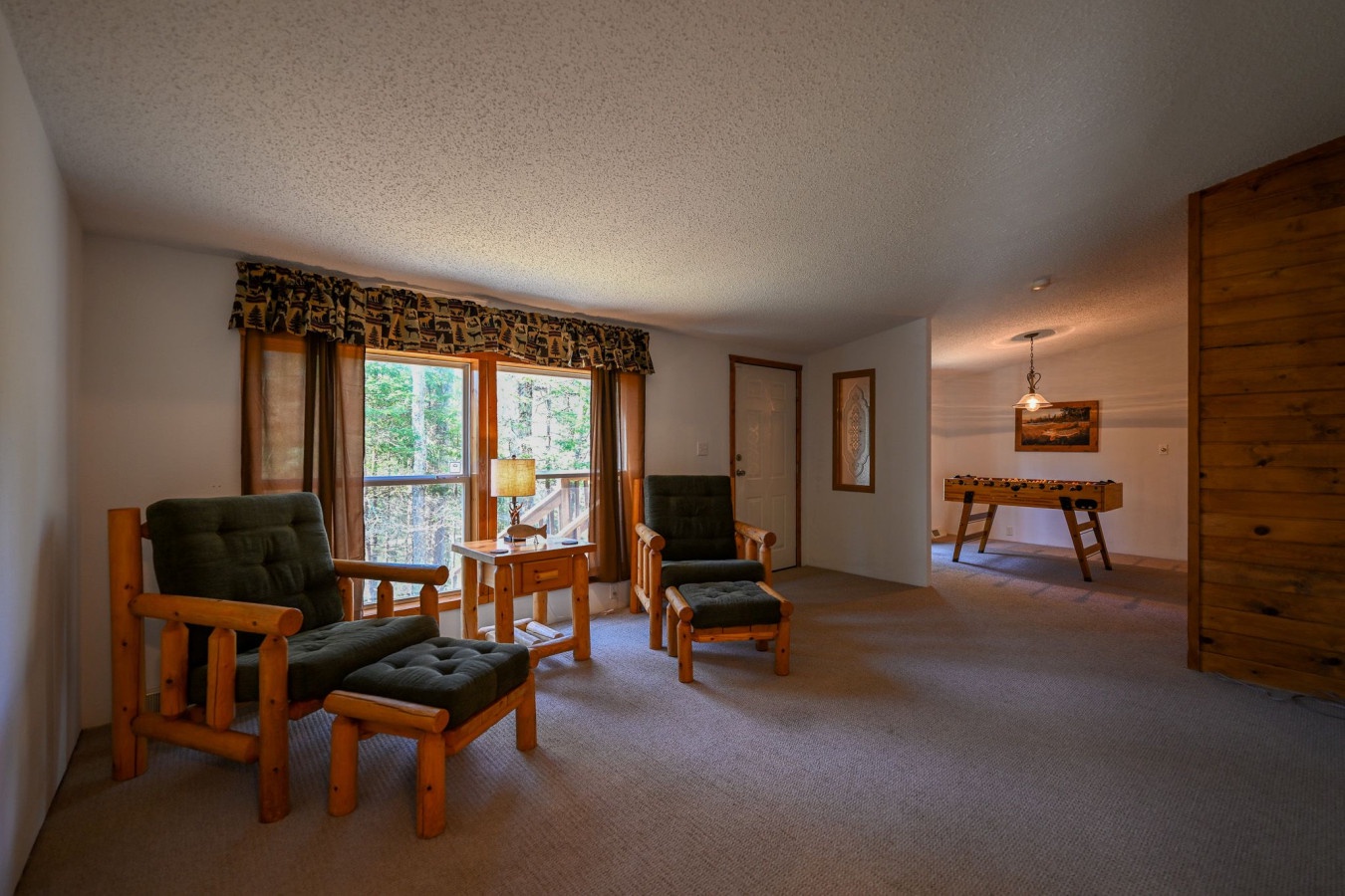 Relax in your cozy living room with rustic wood furniture, where large windows frame forest views and natural light creates the perfect mountain retreat atmosphere.