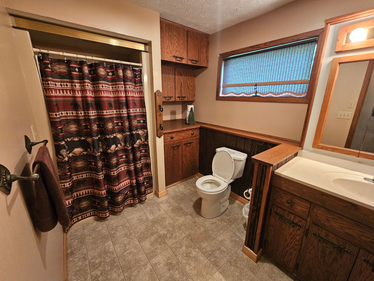 Step into your spacious bathroom featuring rich wood cabinetry, southwestern-style shower curtain, and plenty of storage for all your essentials.