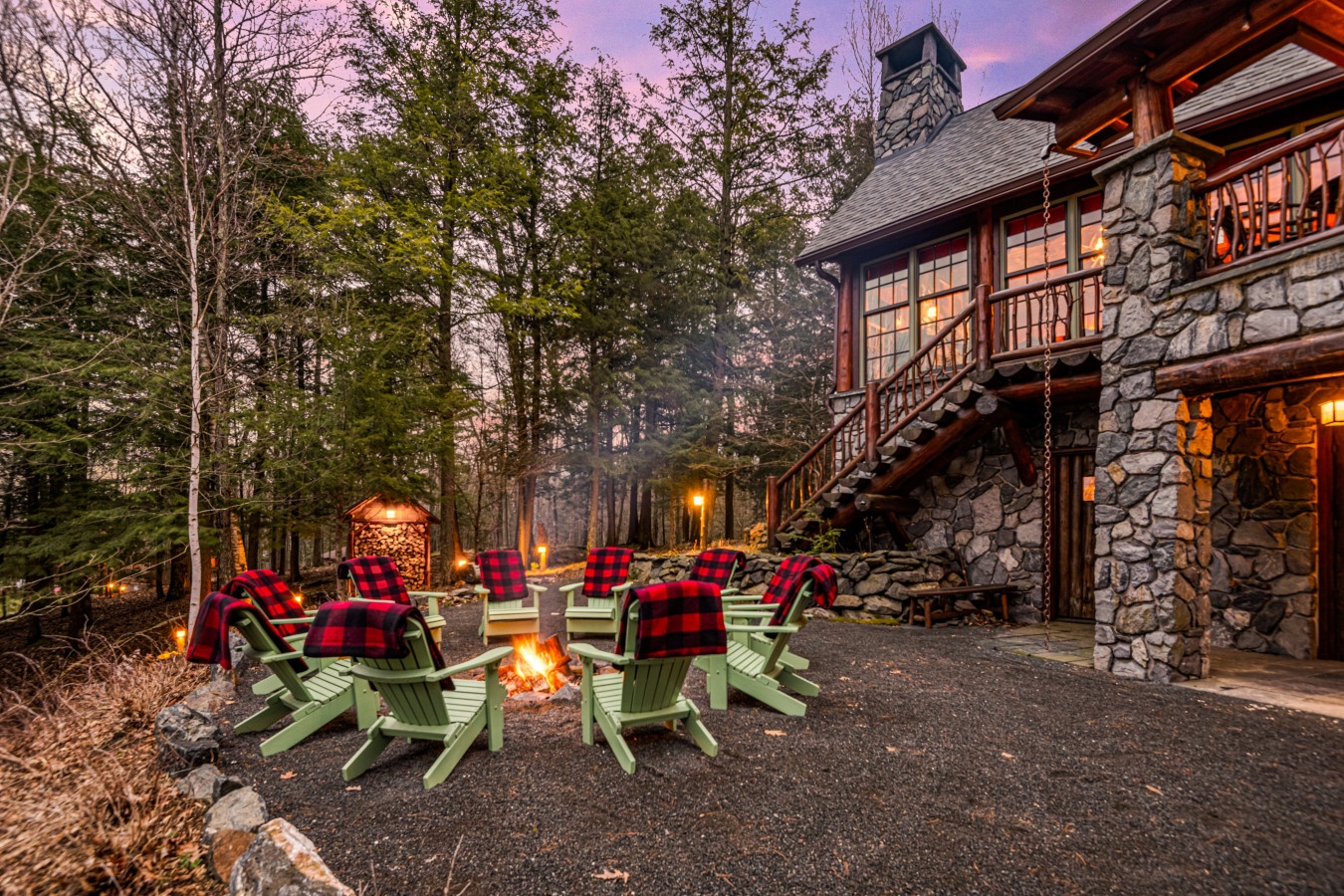 Cozy stone lodge featuring fire pit seating and forest views at dusk.