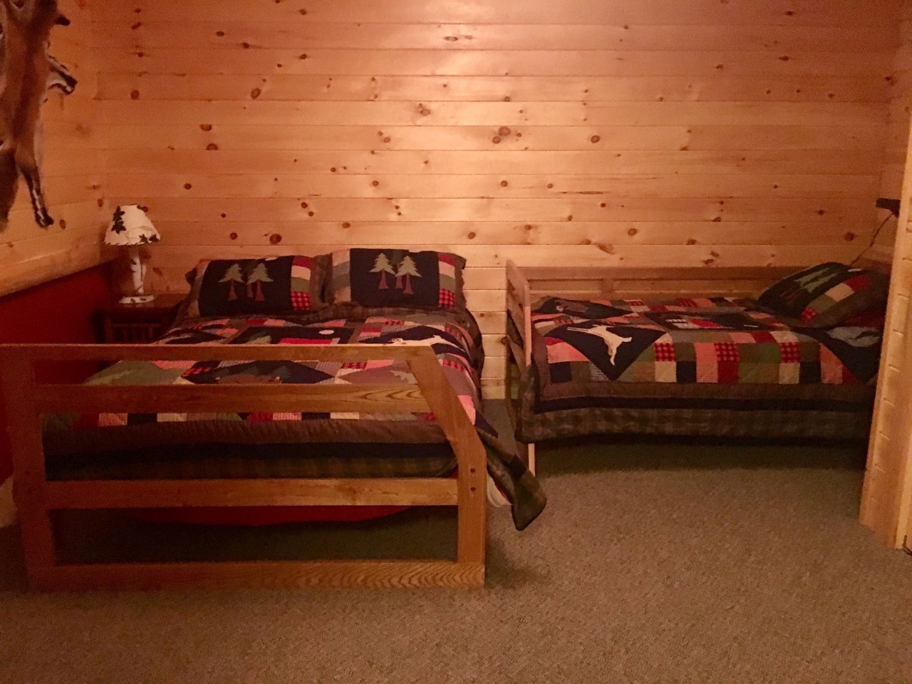 Cozy attic bedroom with rustic pine ceilings and twin beds dressed in charming patchwork quilts featuring festive tree patterns.